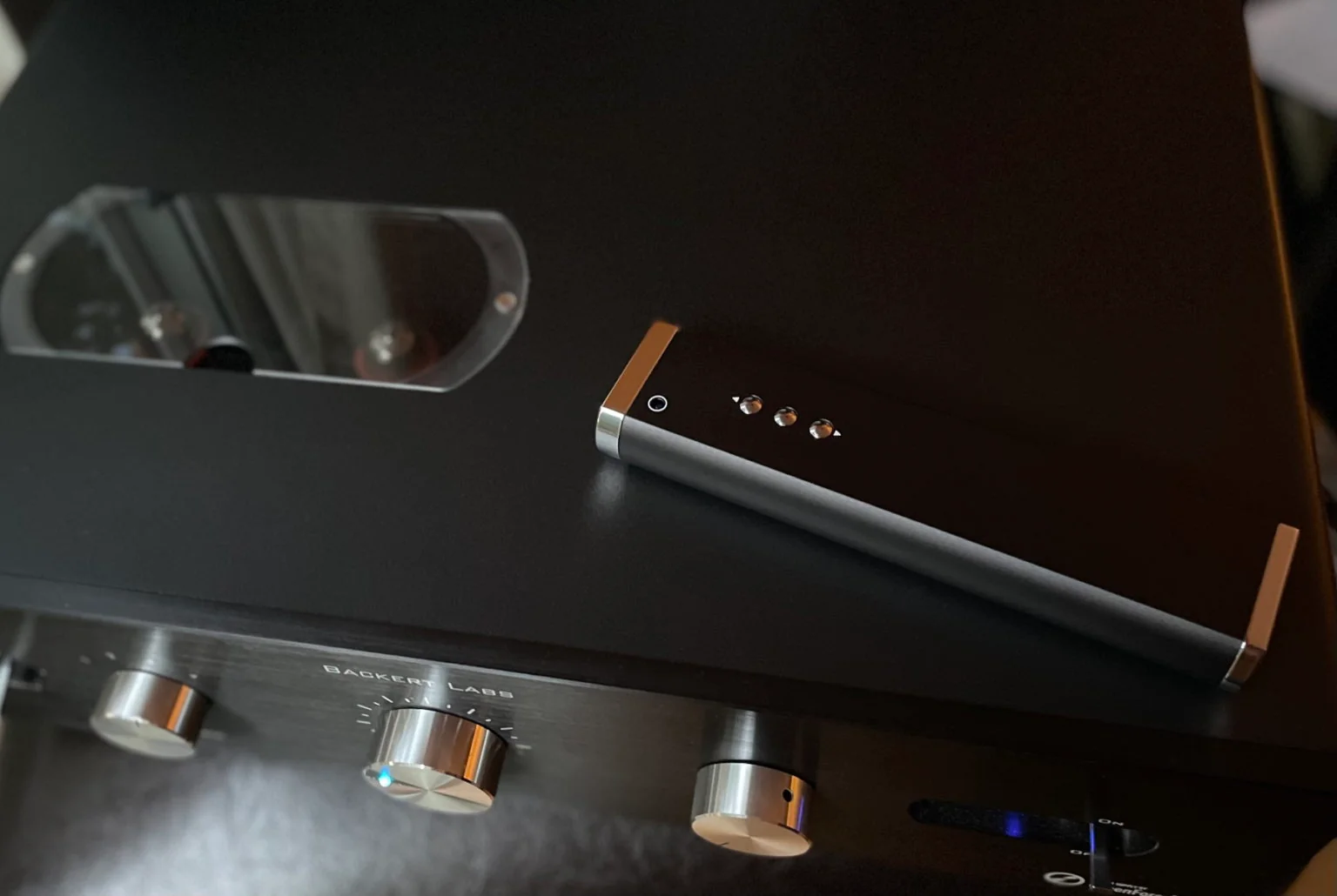 A slim silver remote resting on the black top plate of a Backert Labs preamplifier