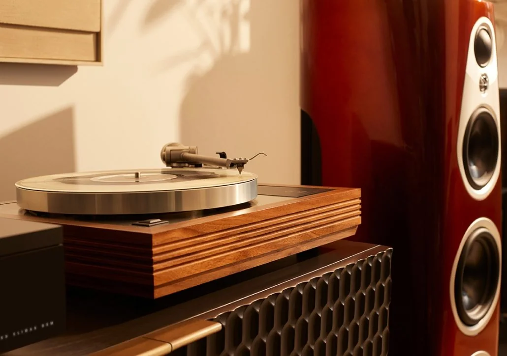 A Linn turntable on a wooden console, a high-gloss red floorstander behind it