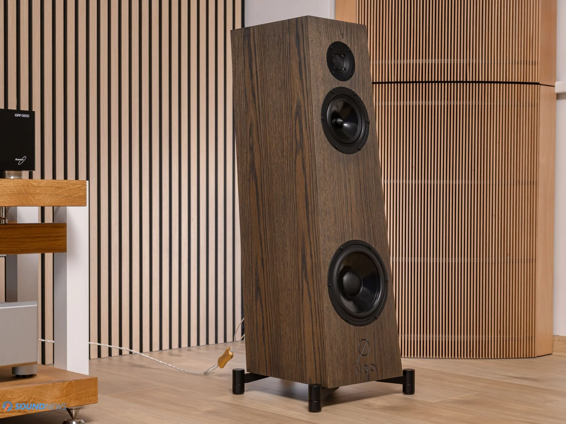 An Ø Audio floorstander in walnut standing in a wood-slatted room
