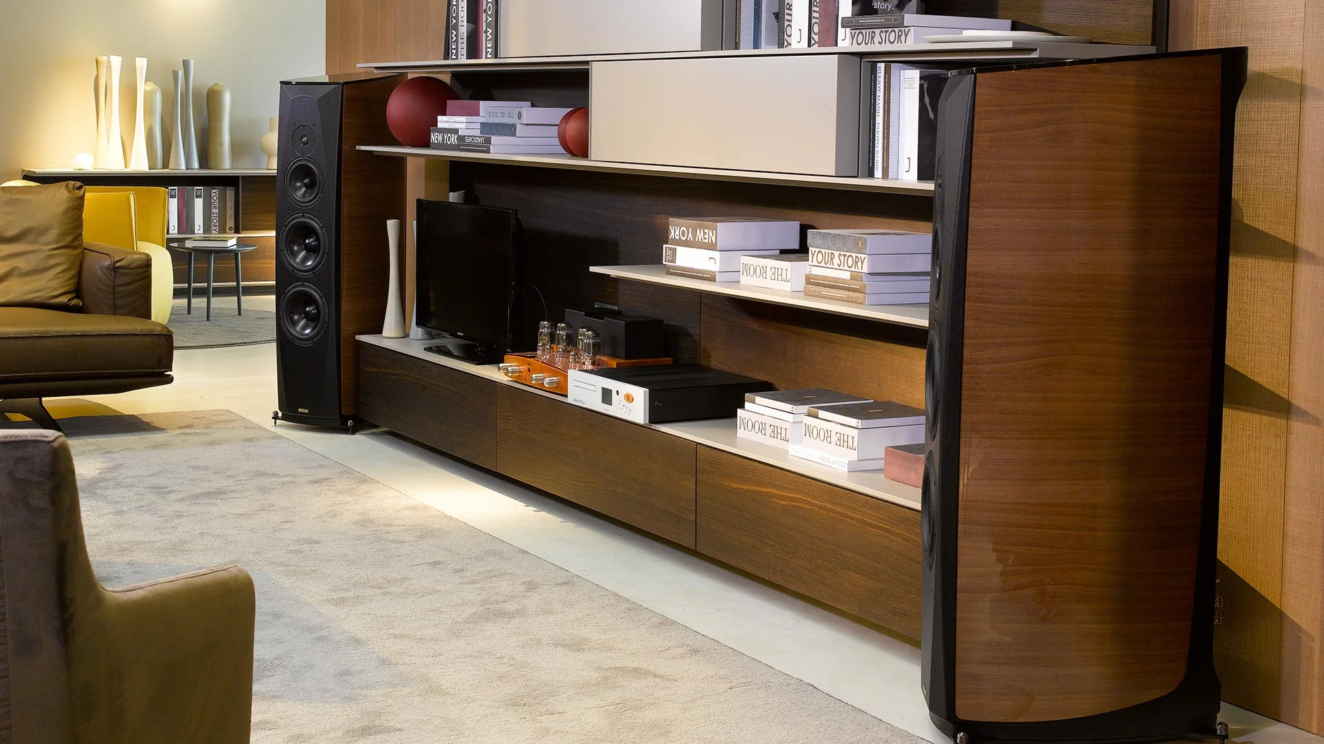 Opera loudspeakers flanking a long walnut console in a carpeted listening room