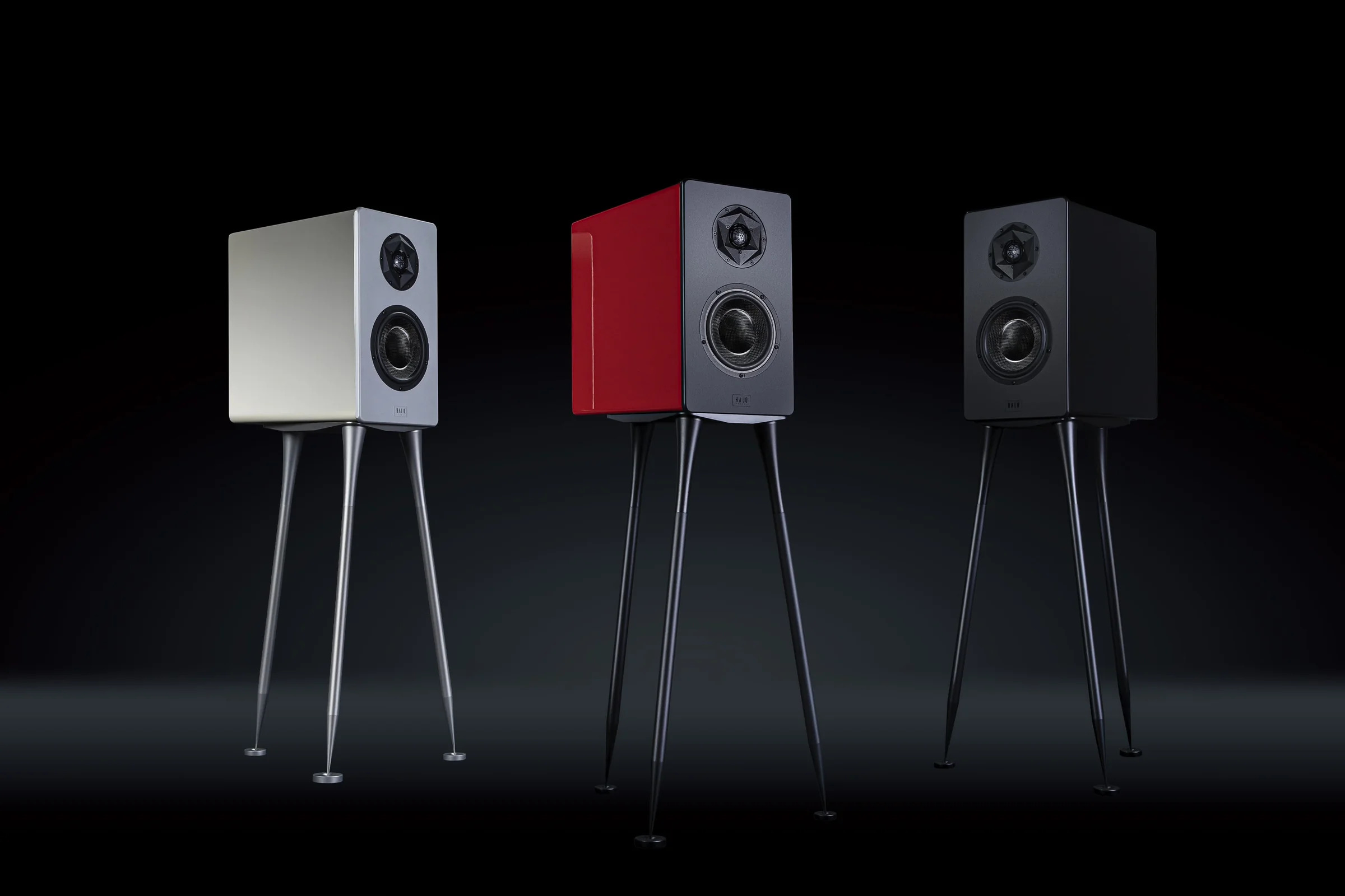 Three Starke Sound monitors on splayed steel legs: silver, red, black