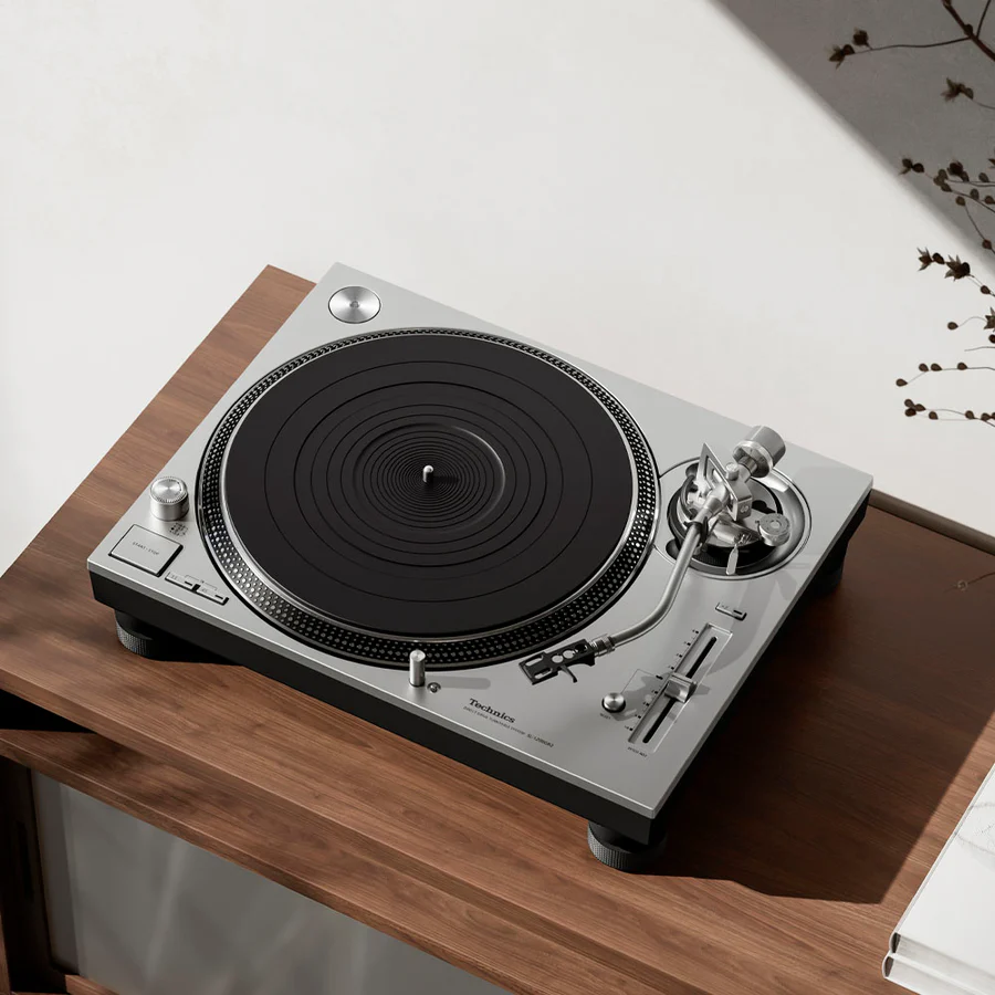 A silver Technics direct-drive turntable on a wooden table
